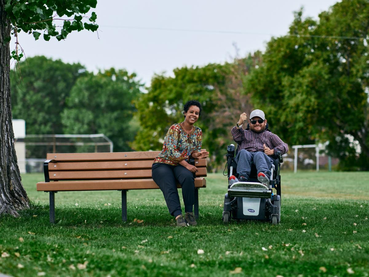 A direct support professional and the person they support sitting on a bench in a park