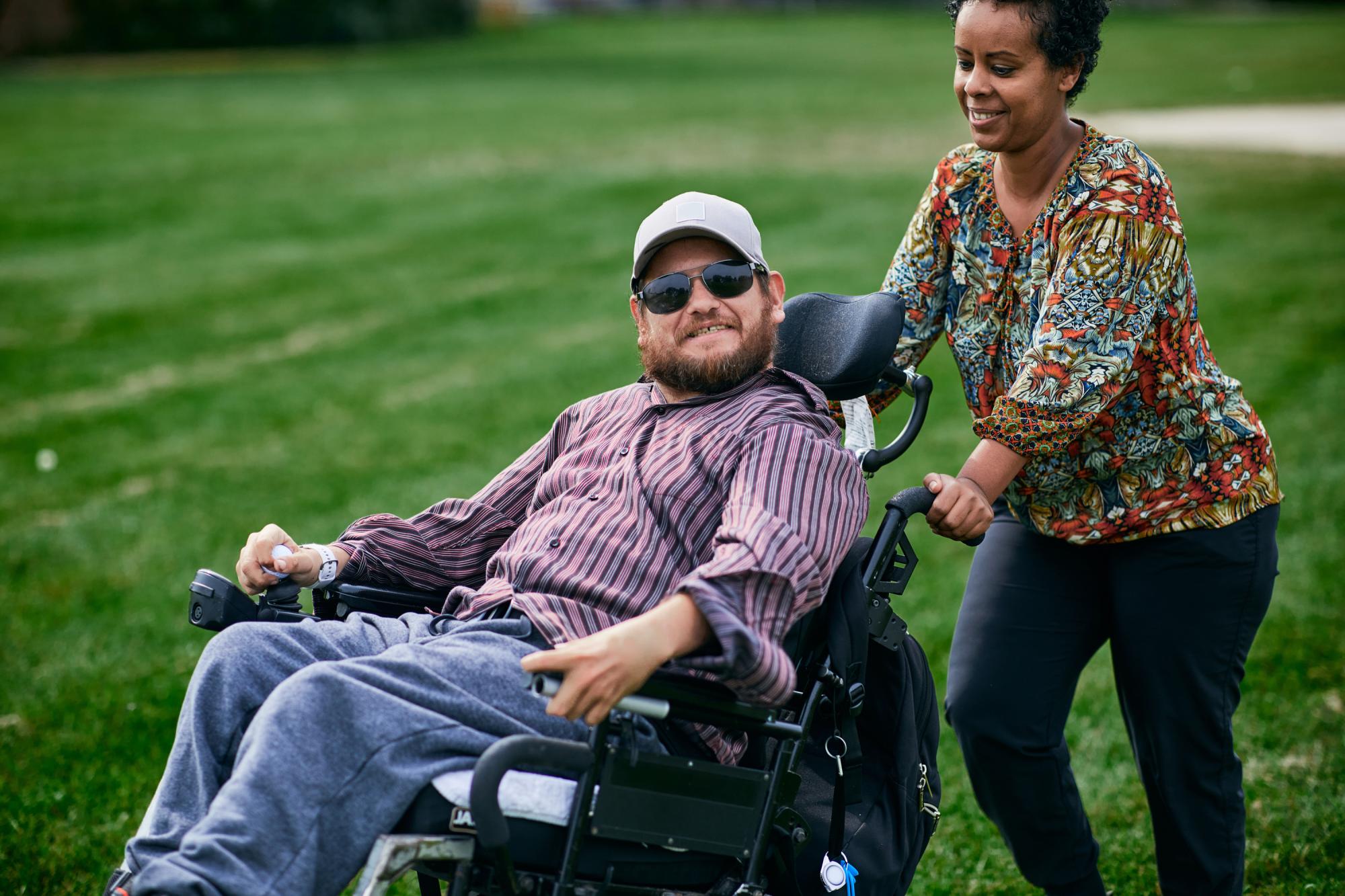 A direct support professional pushing the person they support in a wheelchair