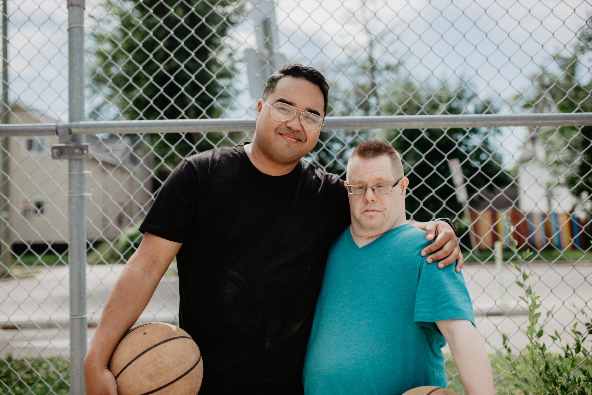 Jose and Cory smiling in front of a basketball court