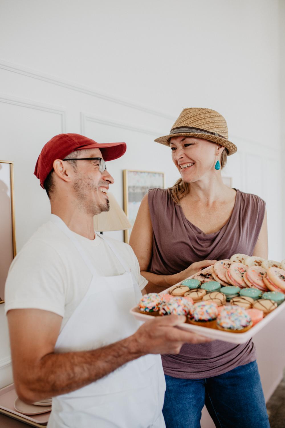 Two people laughing while holding a tray of macaroons